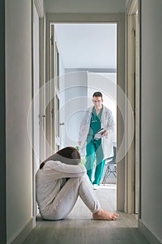 Worried physician running to help mental disorder patient sitting on floor in mental health center