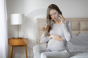 Worried pregnant woman talking on phone at home