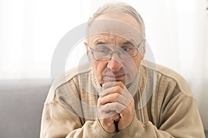 Worried religious senior man praying to god with his hands raised and touching as he looks beseechingly towards heaven