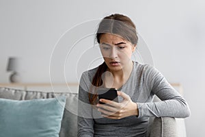 Worried sad shocked depressive attractive young european female looking at phone at home interior