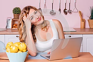 Worried and sad student female searching information in a laptop online sitting in the kitchen. Sad blonde woman feeling