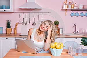 Worried and sad student female searching information in a laptop online sitting in the kitchen. Sad blonde woman feeling