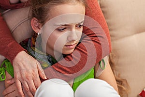 Worried and sad young girl sitting on sofa - woman embracing and comforting her