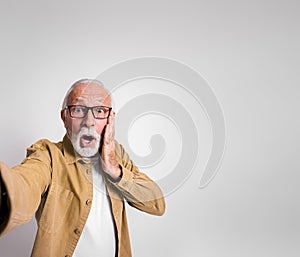 Worried senior businessman touching face and looking at camera in shock against white background