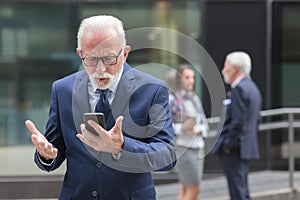 Worried senior businessman using smart phone in front of an office building