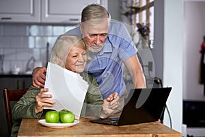worried senior couple checking finances at home using laptop