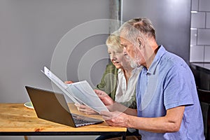 worried senior couple checking finances at home using laptop