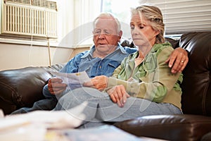 Worried Senior Couple Sitting On Sofa Looking At Bills