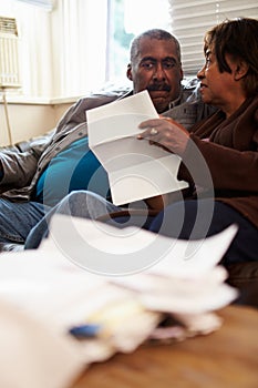 Worried Senior Couple Sitting On Sofa Looking At Bills