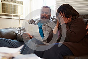 Worried Senior Couple Sitting On Sofa Looking At Bills