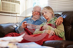 Worried Senior Couple Sitting On Sofa Looking At Bills