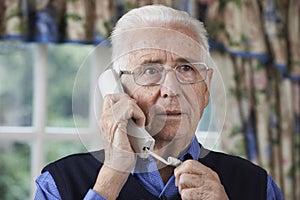 Worried Senior Man Answering Telephone At Home