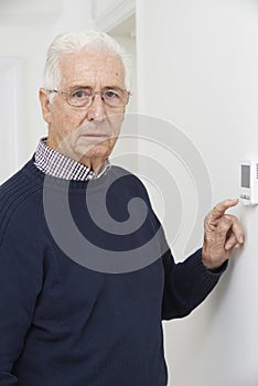 Worried Senior Man Turning Down Central Heating Thermostat