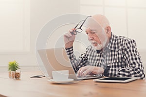 Worried senior man using laptop at home