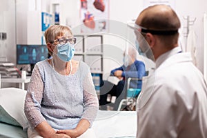 Worried senior woman with face mask looking at doctor