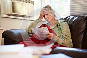 Worried Senior Woman Sitting On Sofa Looking At Bills