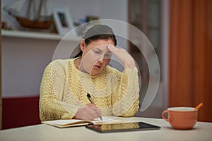 Worried senior woman in yellow sweater writing