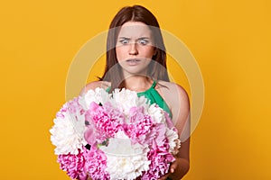 Worried shocked young woman looking at pink and white flowers with surprise, holding peonies in both hands, opening eyes widely,