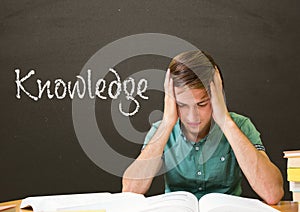 Worried student boy at table against grey blackboard with knowledge text