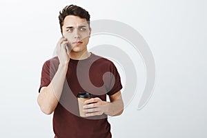 Worried suspicious attractive european man in casual red t-shirt, holding cup of coffee, frowning and looking aside