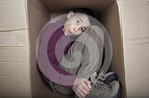 Worried teenage boy sitting in cardboard box