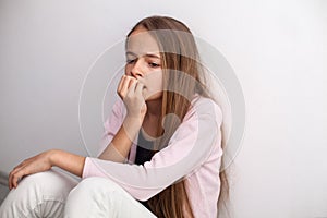 Worried teenage girl biting her nails sitting on the floor by th photo