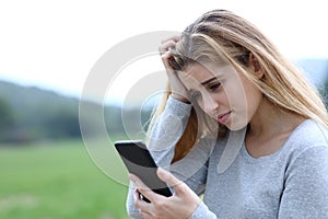 Worried teenage girl checking phone message outdoors