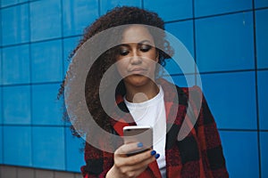 Worried teenager girl looking at her smart phone in a park with an unfocused background