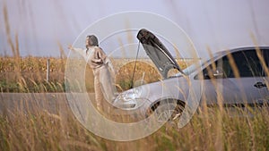 Worried troubled woman hitchhiking standing at broken automobile at autumn field. Wide shot portrait of anxious stressed