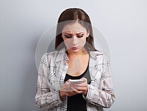 Worried unhappy young woman typing sms and looking on mobile phone