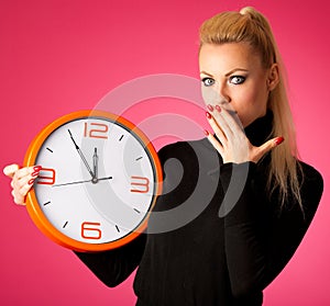 Worried woman with big orange clock gesturing delay, rush, nervous, stress because of lack of time.