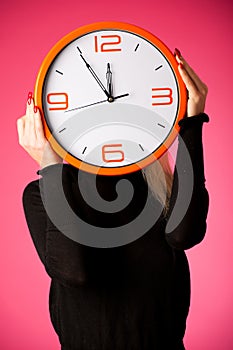 Worried woman with big orange clock gesturing delay, rush, nervous, stress because of lack of time.