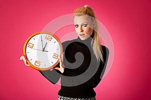 Worried woman with big orange clock gesturing delay, rush, nervous, stress because of lack of time.