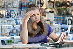 Worried Woman Checking Bills And Invoices In Computer Shop