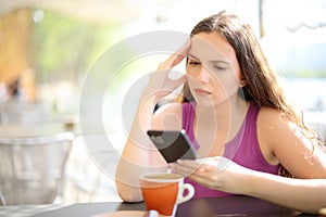 Worried woman checking phone in a bar terrace