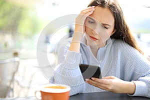 Worried woman checking phone in a restaurant terrace