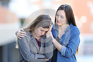 Worried woman comforting her sad friend in the street photo
