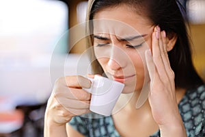 Worried woman drinking coffee suffering head ache