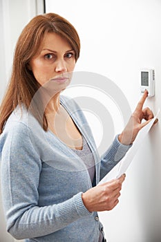 Worried Woman With Heating Bill Turning Down Thermostat