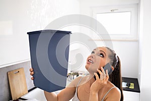 Woman Holding Bucket While Water Droplets Leak From Ceiling