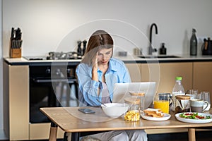 Worried woman housewife looking at laptop screen touching head