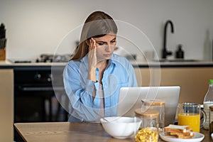 Worried woman housewife looking at laptop screen touching head