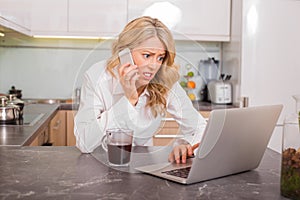 Worried woman in kitchen working on computer