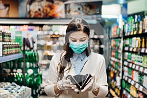 Worried woman with mask groceries shopping in supermarket looking at empty wallet.Not enough money to buy food.Covid-19 quarantine