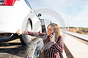 Worried woman on the phone and touching the flat tire of her car on a tow truck