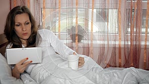 Worried woman reading bad news in tablet computer and drink morning coffee tea