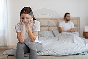 Worried woman sitting on bed with man sitting in background