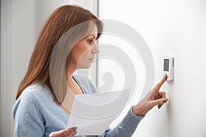 Worried Woman Turning Down Central Heating Thermostat