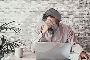 Worried worker man touching his front with thoughts sitting in front of on open laptop. Computer online modern job and problems.