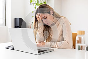 Worried young adult woman using laptop at home